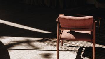 Une chaise dans une pièce faiblement éclairée, avec un tapis à motifs et un rideau en arrière-plan.