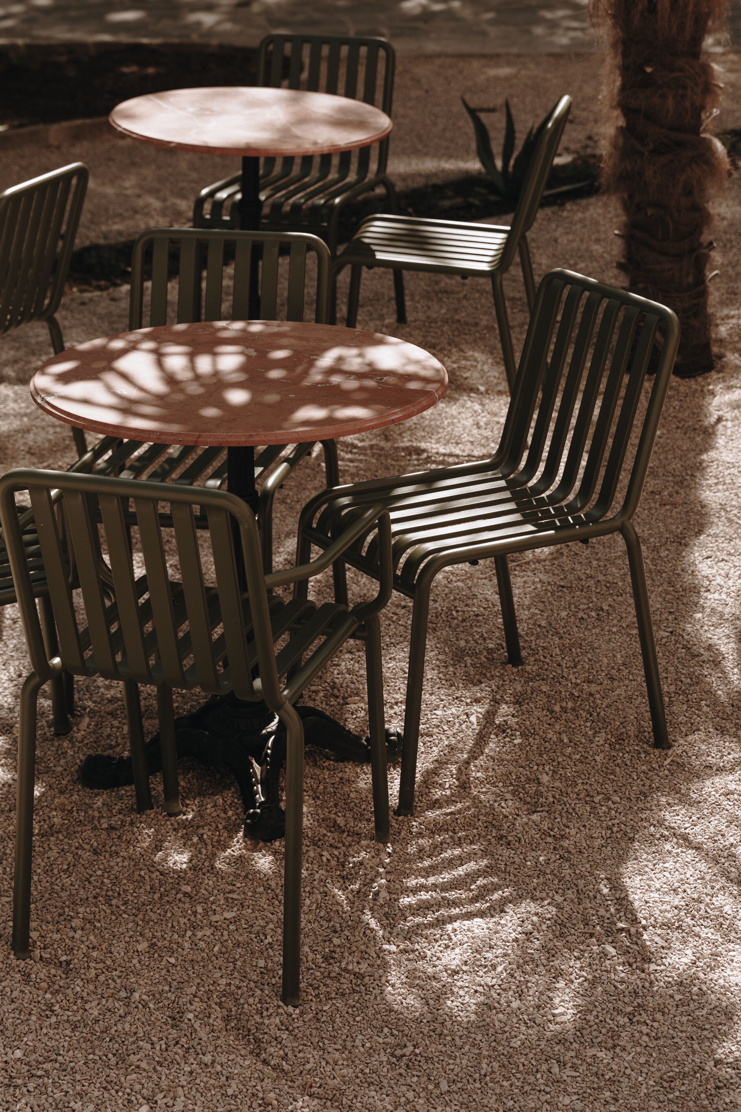 Een zithoek met ronde tafels en metalen stoelen, buiten op een grindpad.