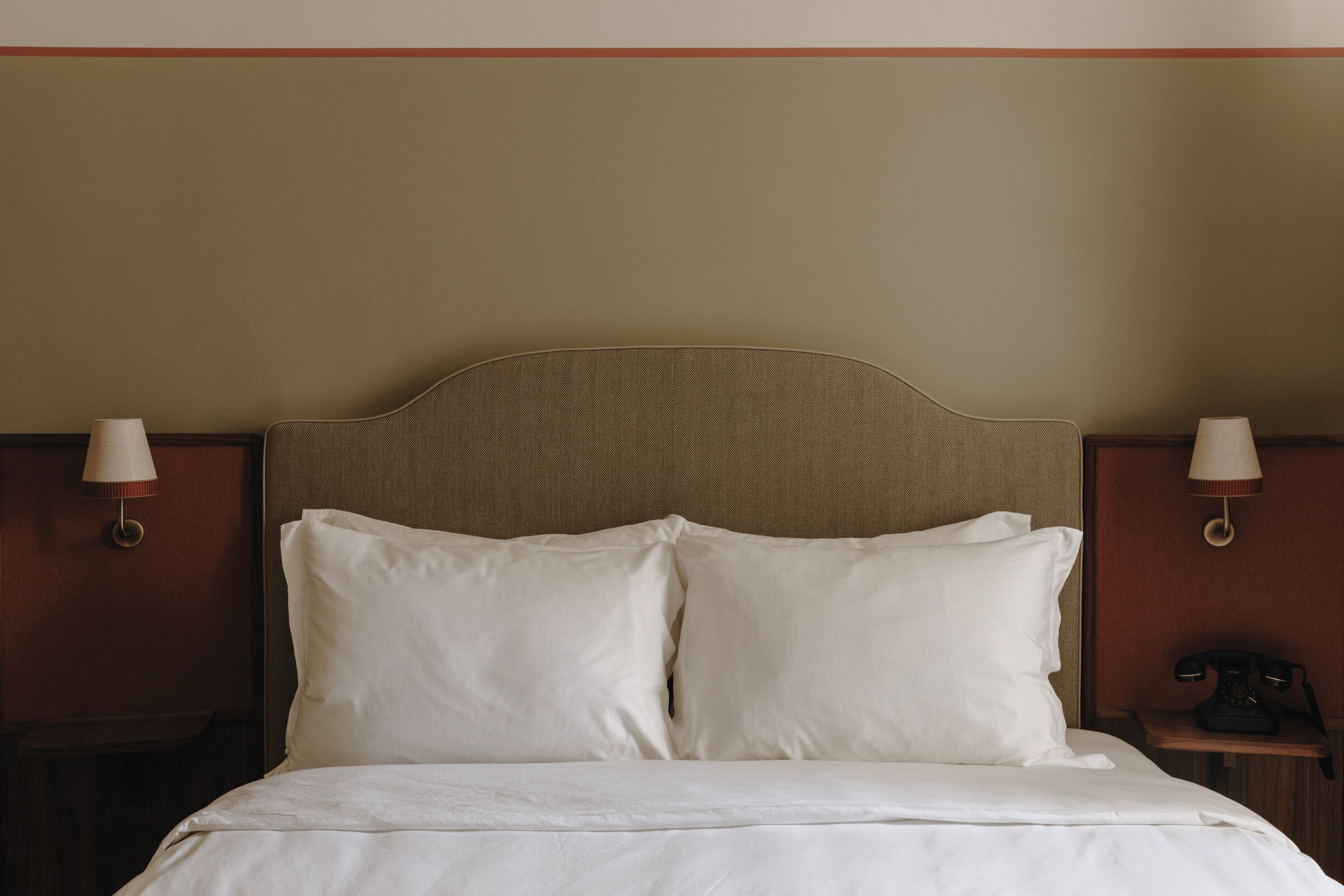 A neatly made bed with white linens, a wooden headboard, and two bedside lamps on wooden nightstands.