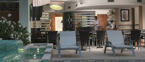 A poolside area with lounge chairs, a bar, and a kitchen visible in the background.