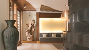 A modern living room with a sofa, a large vase, and a wooden sculpture.