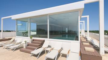 Une terrasse moderne avec une piscine, des chaises longues et un grand mur de verre offrant une vue sur la ville.