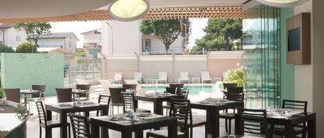 Un restaurante con terraza, vistas a la piscina y diseño de interiores moderno.