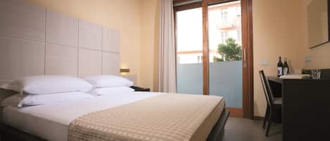 A hotel room with a bed, a desk, and a view of the outside balcony.