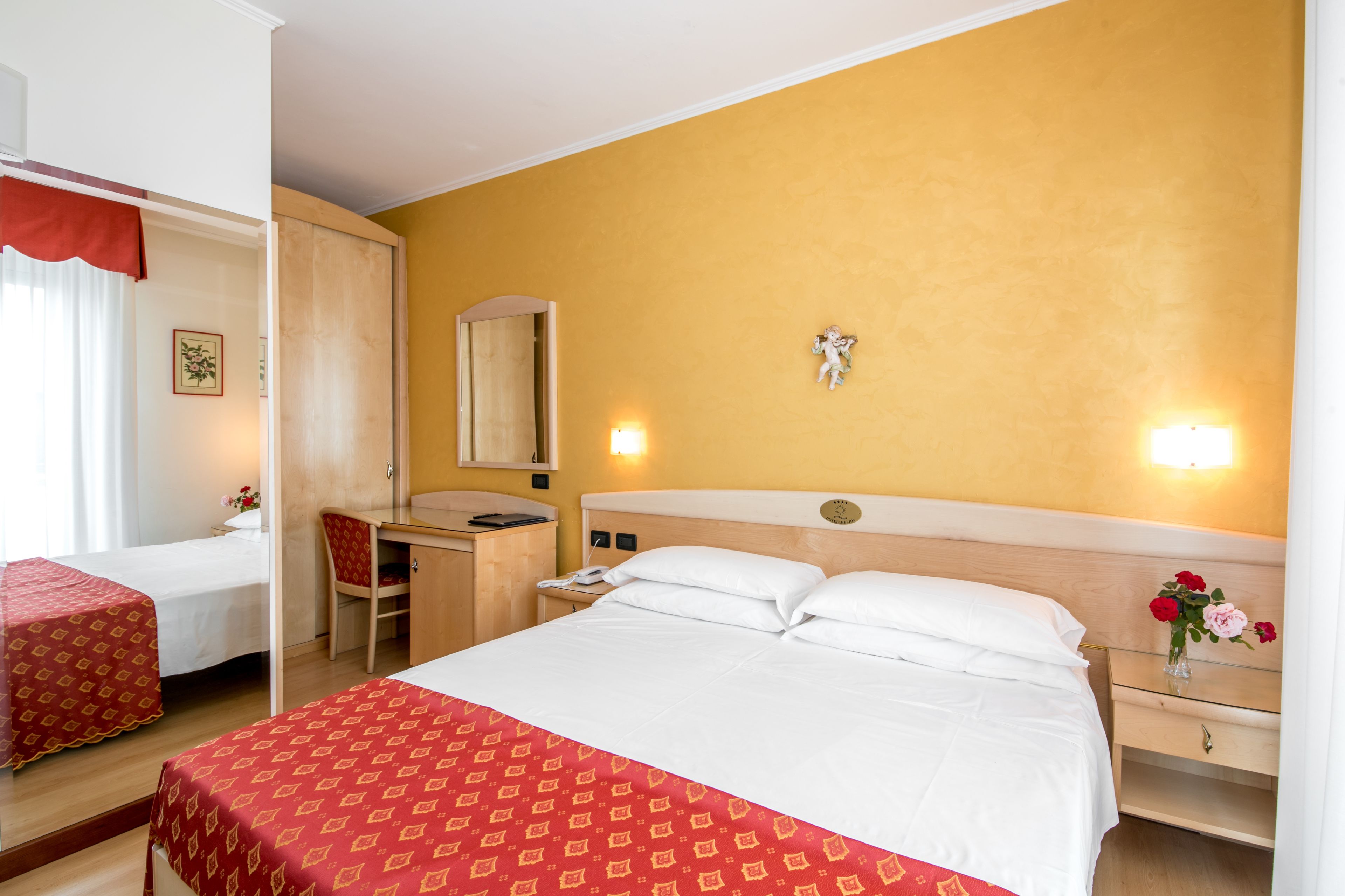 A hotel room with a large bed, a desk, a chair, and a small table with a vase of flowers.