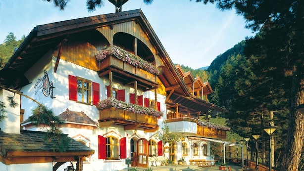 Un edificio de estilo alpino tradicional con balcones de madera y contraventanas rojas, rodeado por un patio con mobiliario para exteriores.