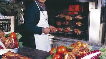 Un chef asando carne al aire libre, con un entorno rústico y un horno de leña al fondo.