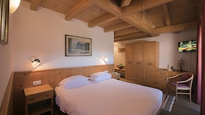 Un dormitorio con techo de madera, una cama con ropa de cama blanca, una mesita de noche, un aparador, una silla y un televisor en la pared.