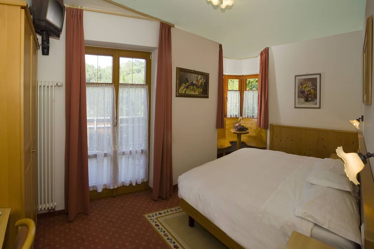 A bedroom with a bed, a wooden wardrobe, a desk with a telephone, and a window with curtains.