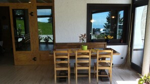 A wooden dining table with four chairs, a bench, and a window with a view of a green landscape. - Piccolo Hotel Sciliar (Castelrotto)