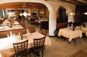 Un restaurante con varias mesas dispuestas para comer, sillas de madera y lámparas colgantes.