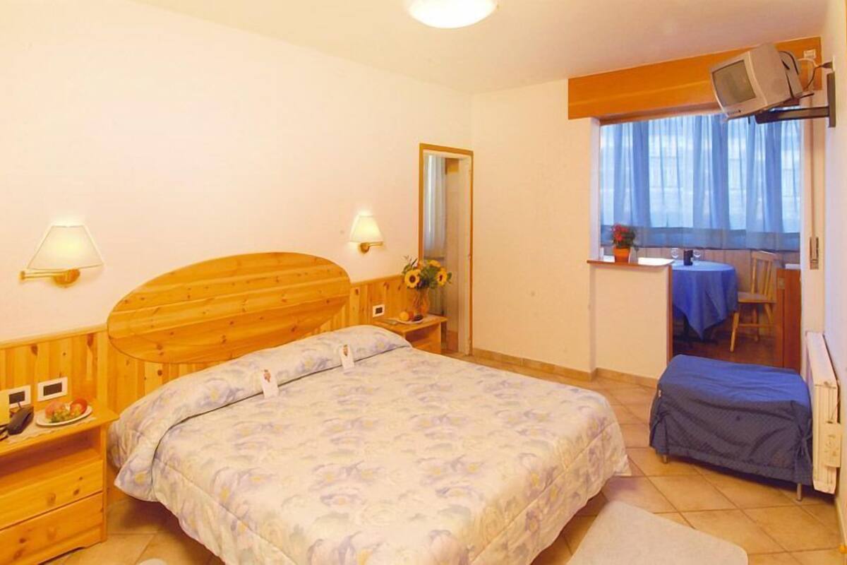 A bedroom with a wooden bed, bedside tables, a small desk, a chair, and a television mounted on the wall.