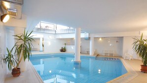 An indoor swimming pool with clear blue water, surrounded by white walls and columns, with potted plants and white chairs. - Piccolo Hotel Sciliar (Castelrotto)