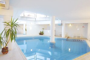 Una piscina interior con baldosas azules cristalinas, pilares blancos y plantas en macetas.