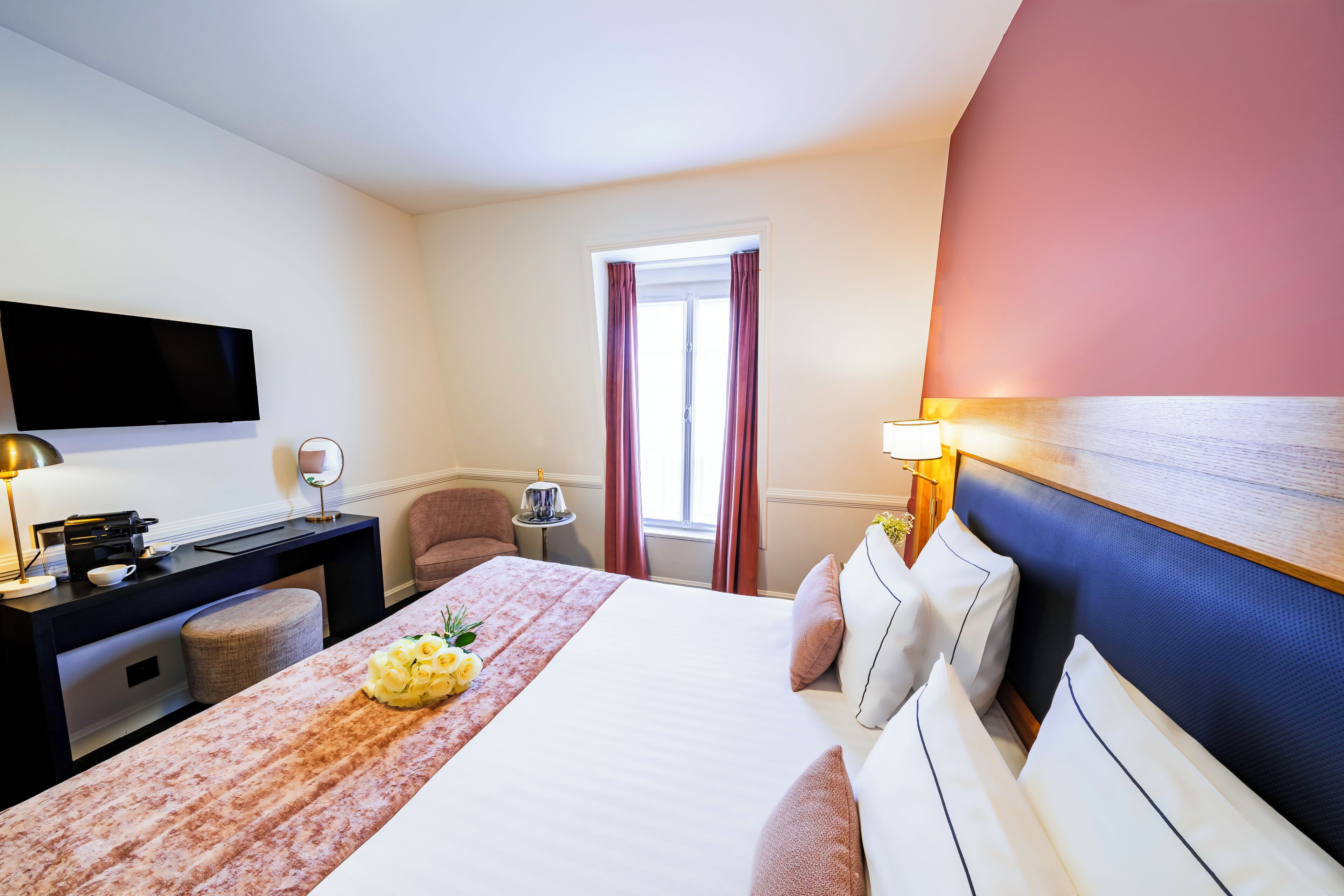 A hotel room with a bed, a desk with a computer, a chair, and a window with curtains.