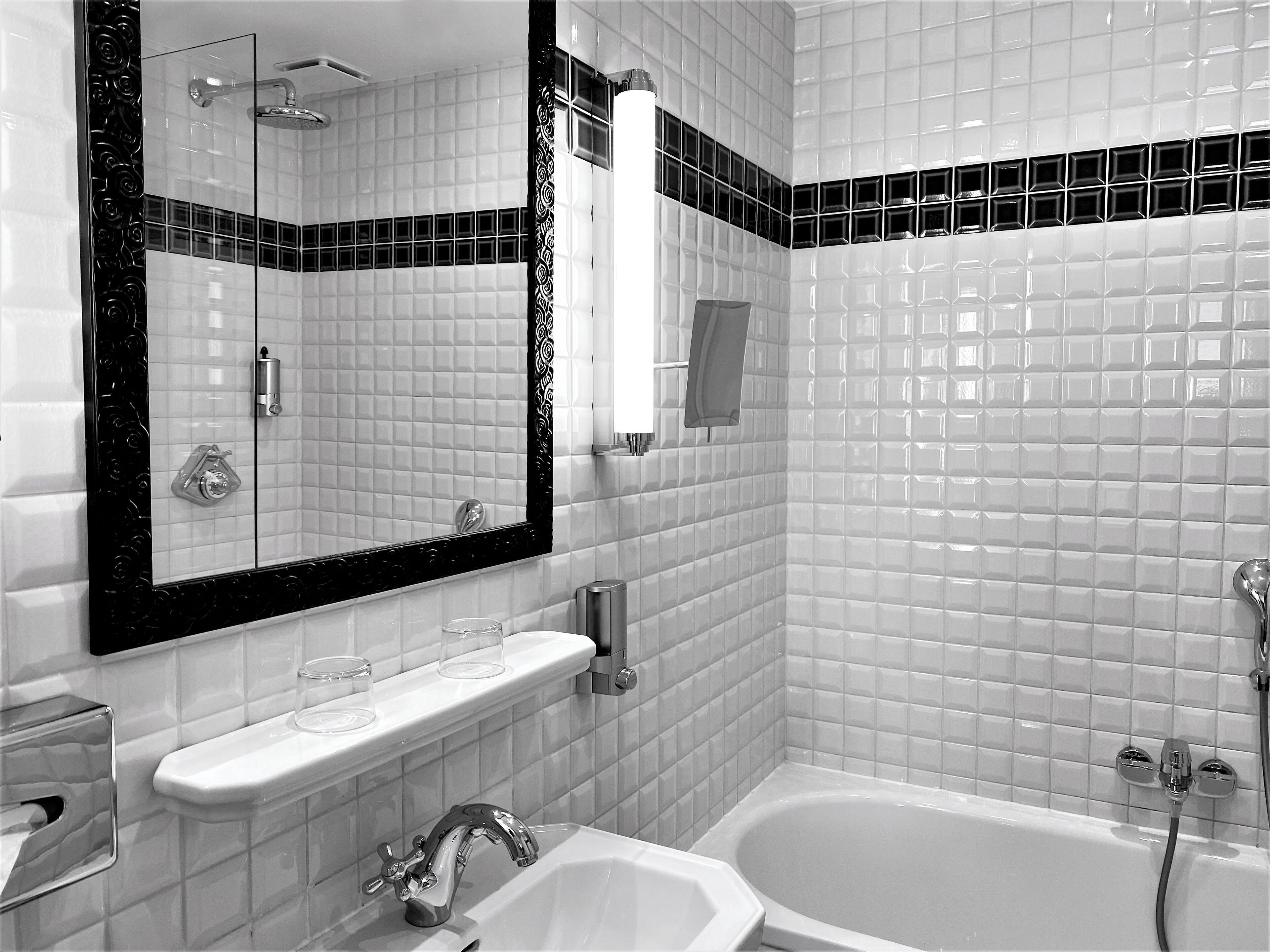 A modern bathroom with a large mirror, a bathtub, and a sink with a glass of water on the counter.