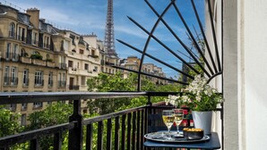 A balcony with a table set for two, overlooking a cityscape with historic buildings and the Eiffel Tower in the background. - Hotel Le Cercle Tour Eiffel (Paris)