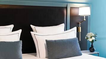 Ein ordentlich gemachtes Bett mit weißen und grauen Kissen, einem dunklen Kopfteil und einem Nachttisch mit Lampe und Blumen.
