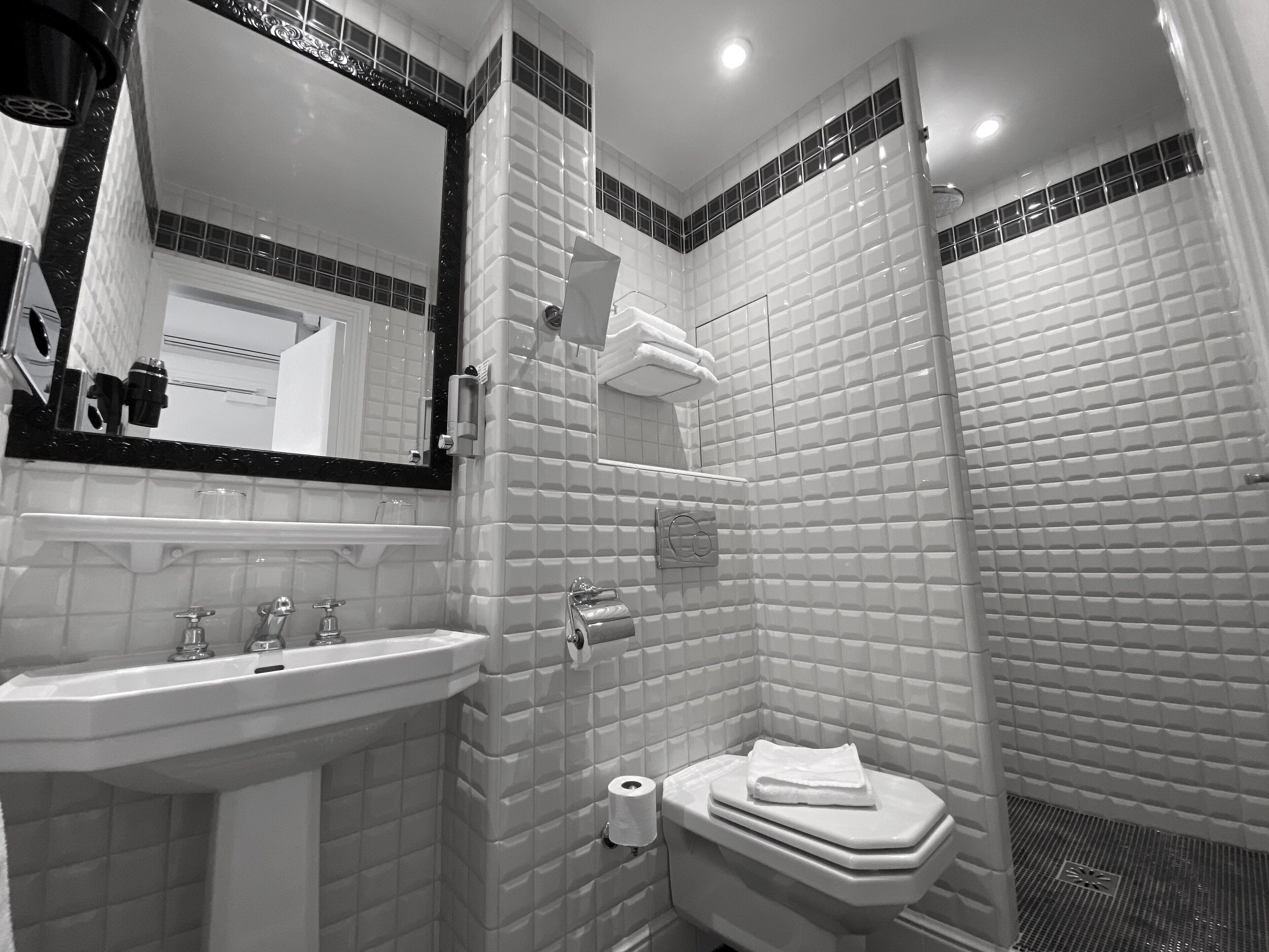 Une salle de bain moderne avec un lavabo blanc, un miroir et des toilettes, ainsi qu’un espace douche aux murs carrelés.