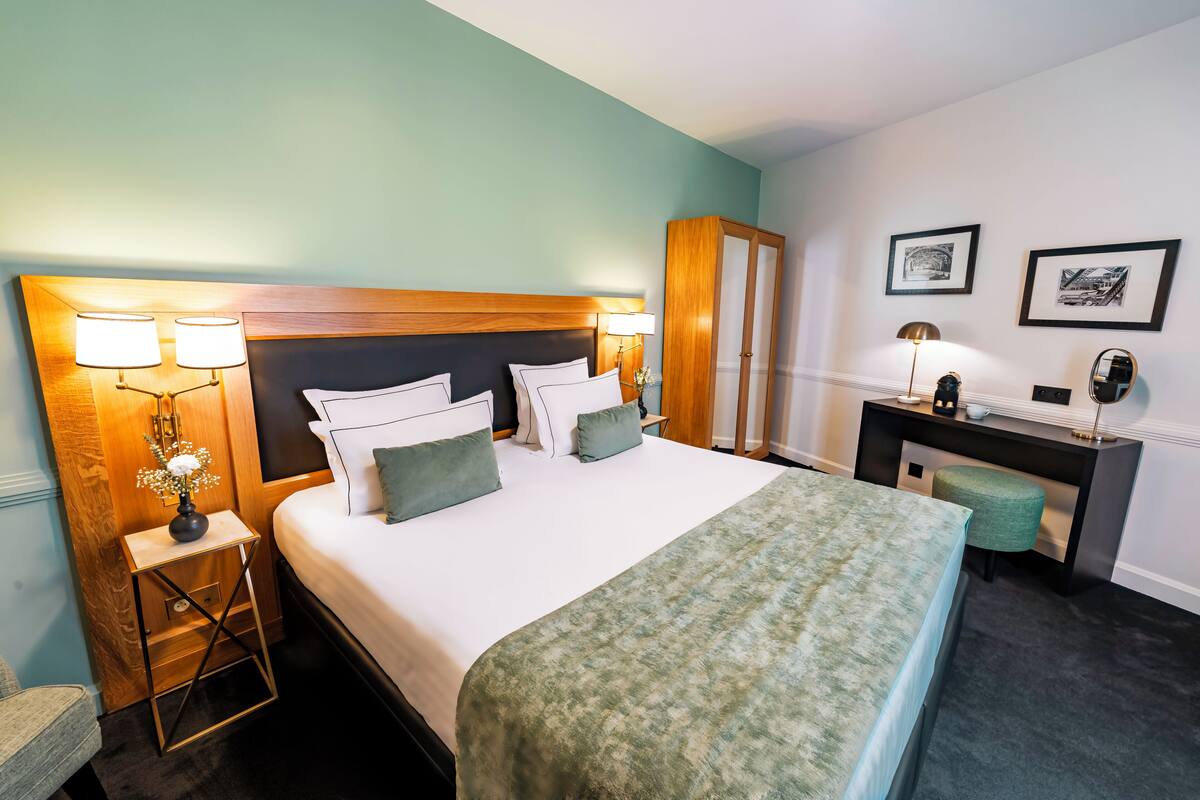 A neatly arranged hotel room with a bed, bedside lamps, a desk, and a chair.