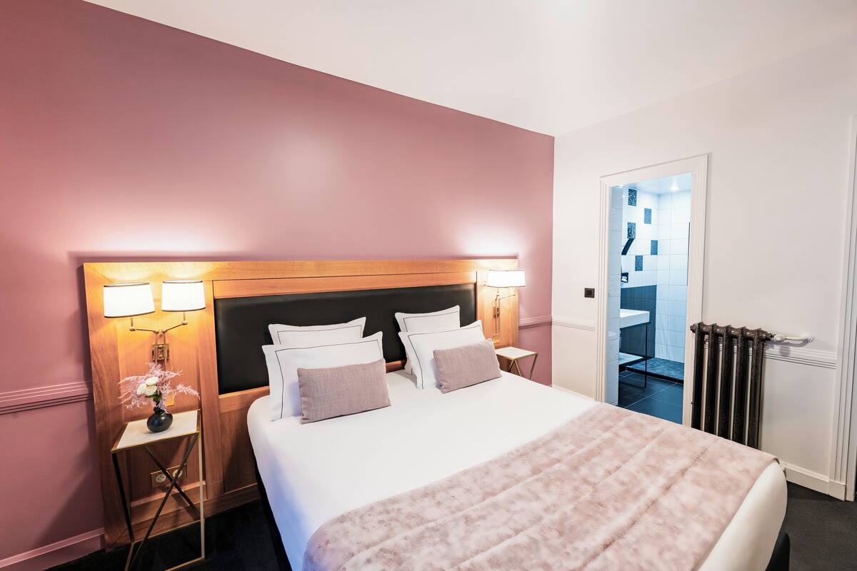 A hotel room with a large bed, bedside lamps, a nightstand, and a view of the bathroom.