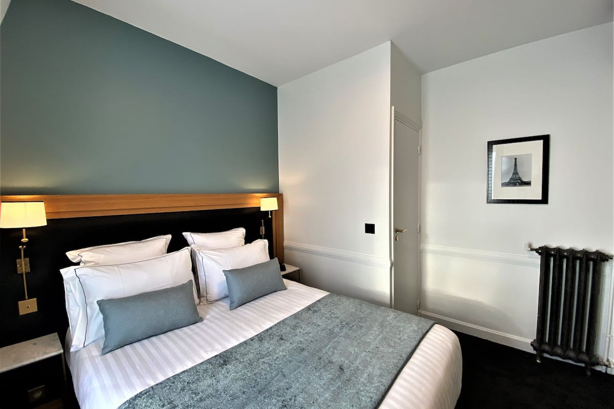 A neatly made bed with white and grey bedding, a wooden headboard, and a blue accent wall.