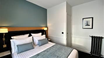Un lit bien fait, avec une literie blanche et grise, une tête de lit en bois et un mur d’accent bleu.