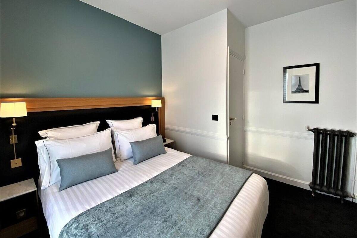 A hotel room with a bed, two bedside lamps, a framed picture on the wall, and a radiator.