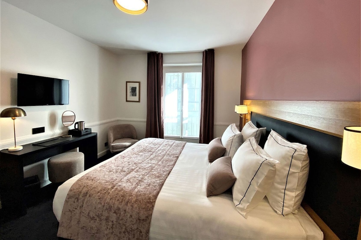 A hotel room with a bed, a desk, a television, and a window with curtains.