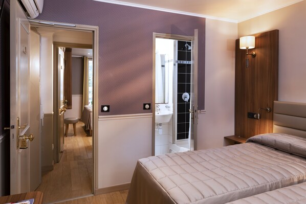 Habitación de hotel con cama, baño con ducha y puerta que da a otra habitación.