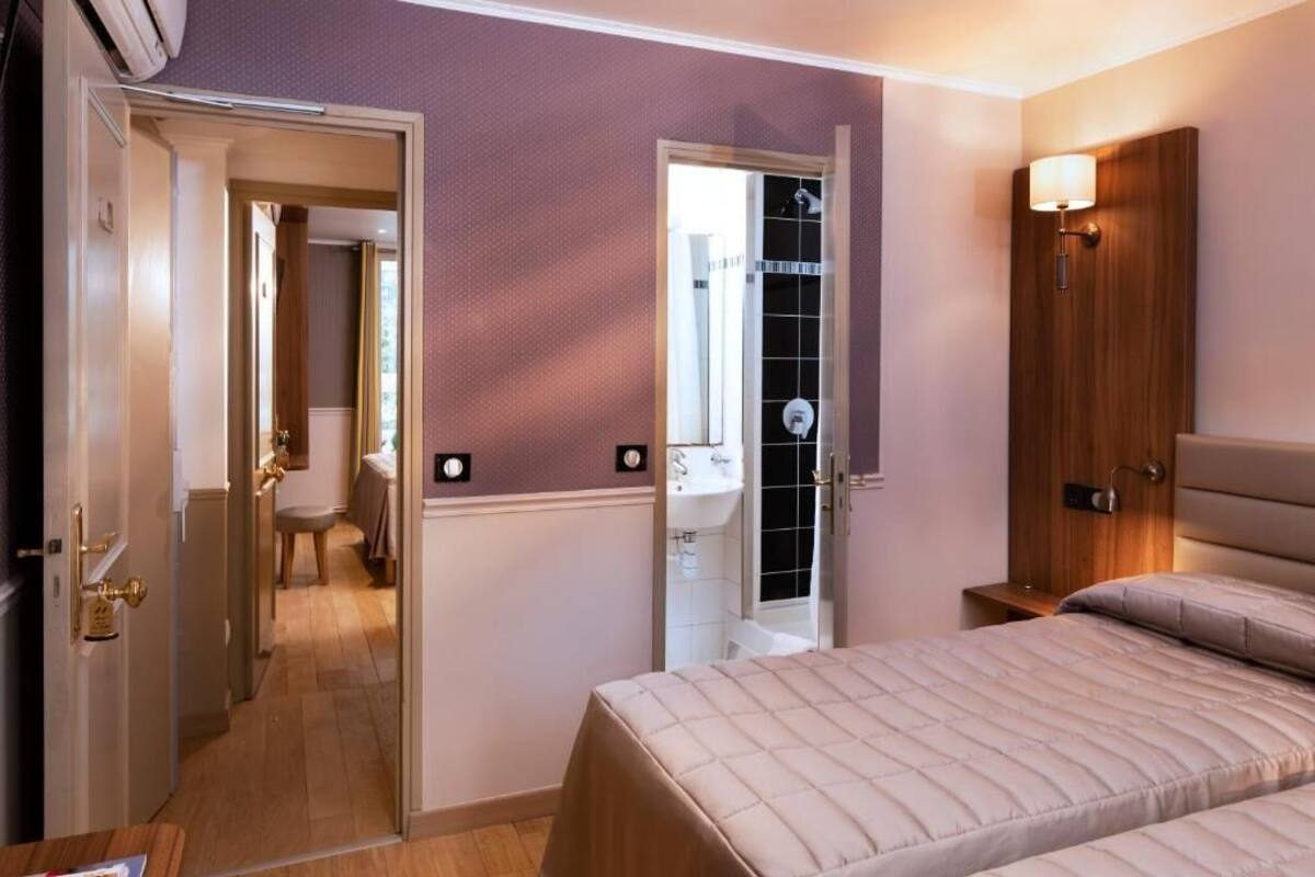A hotel room with a bed, a bathroom with a shower, and a door leading to another room.