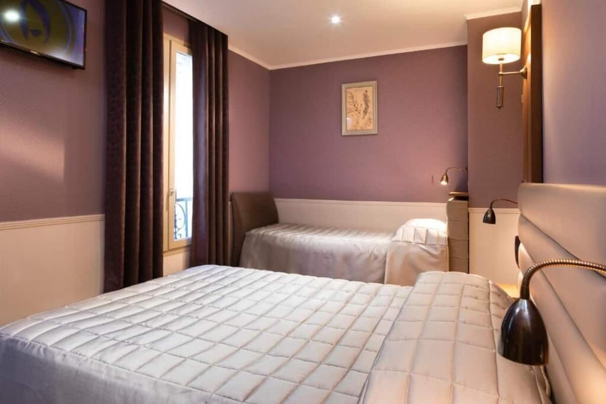 A hotel room with two beds, a window with curtains, a painting on the wall, and a lamp on the nightstand.