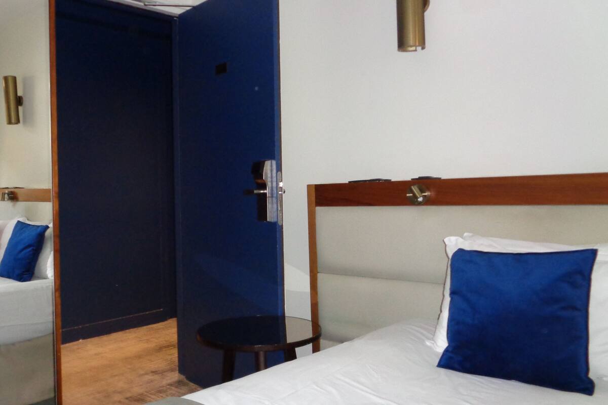 Una habitación de hotel con una cama, una mesita redonda pequeña, una puerta azul y una pared blanca.