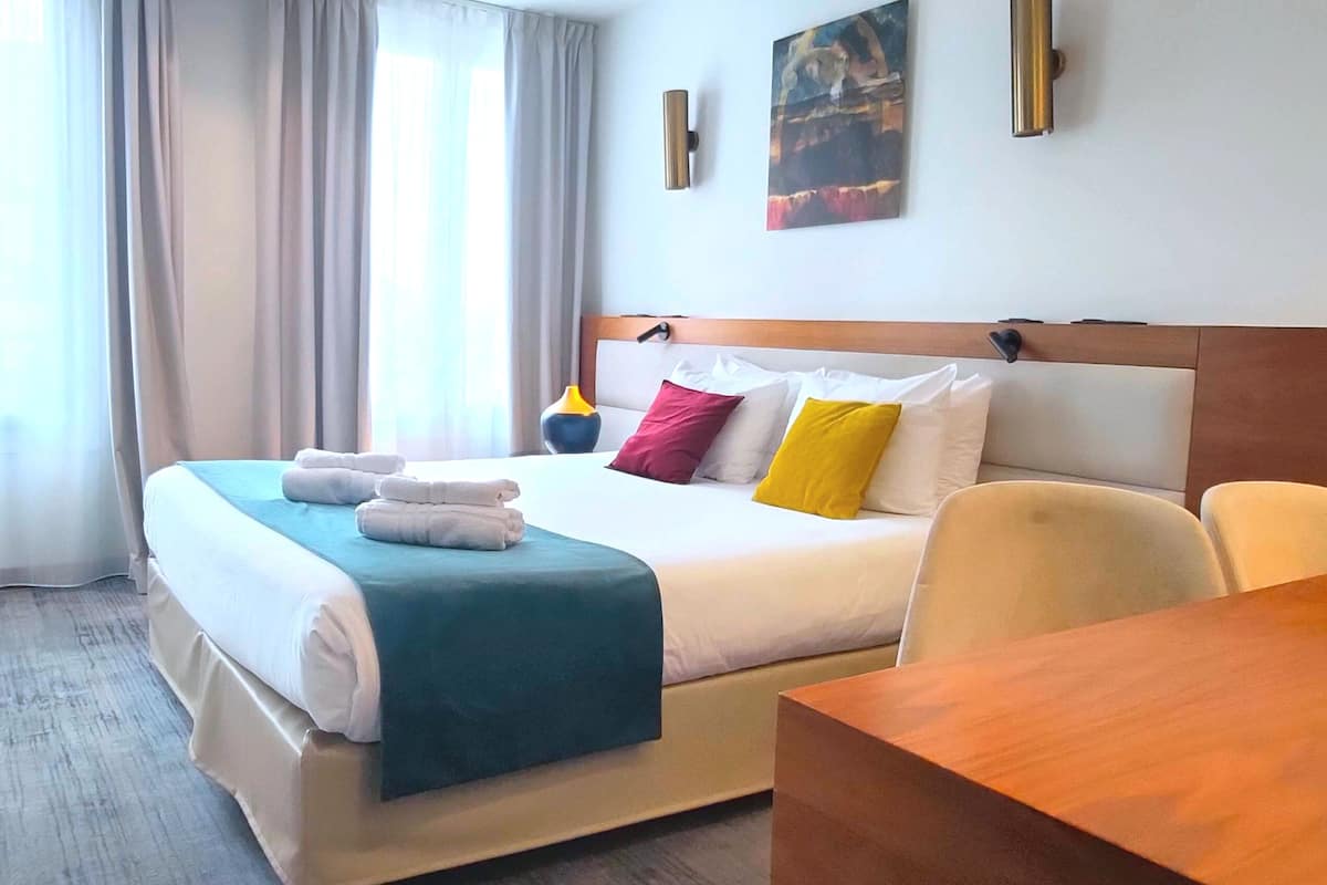 Una habitación de hotel con una cama, cabecero de madera, mesita de noche y una silla.