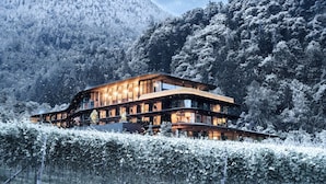 A modern, multi-story building with large windows, surrounded by snow-covered trees and mountains. - Prinz Rudolf Smarthotel (Merano)