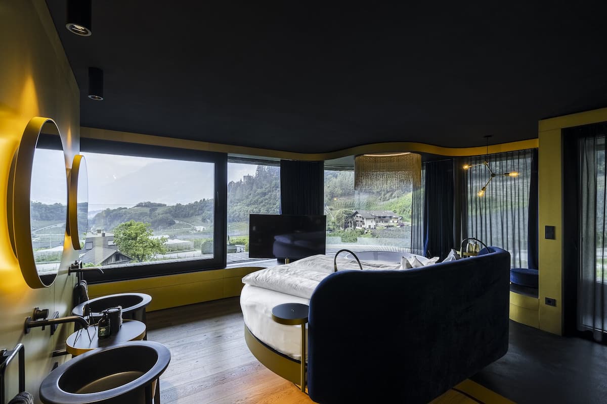 Camera da letto moderna con un letto grande, un divano curvo, un tavolino e un'ampia finestra con vista panoramica.