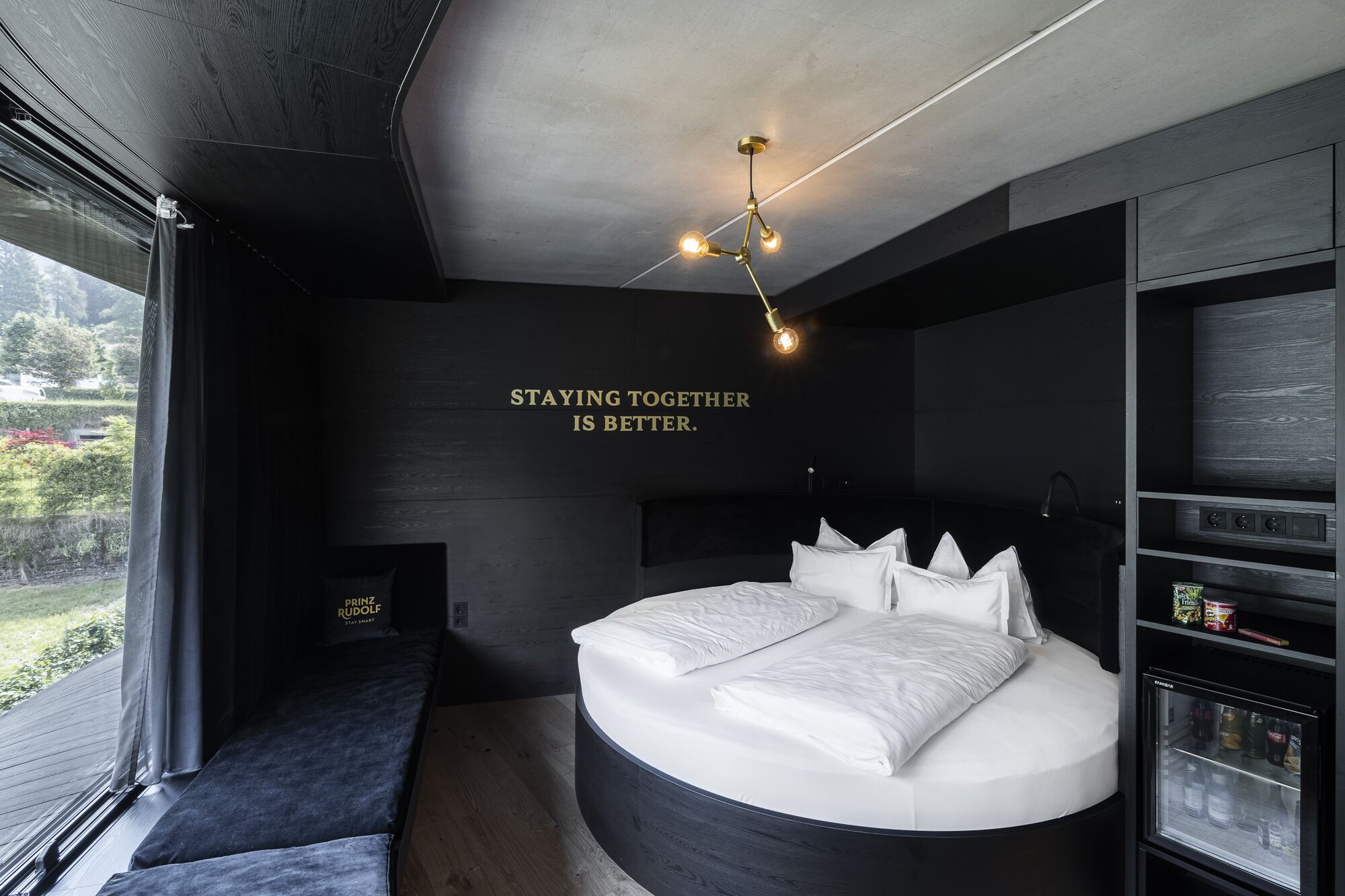A modern bedroom with a large bed, a built-in bench, a wall-mounted TV, and a statement "STAYING TOGETHER IS BETTER."
