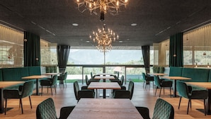 A modern restaurant interior with a high ceiling, exposed ductwork, and a central chandelier. Tables and chairs are arranged for dining. - Prinz Rudolf Smarthotel (Merano)