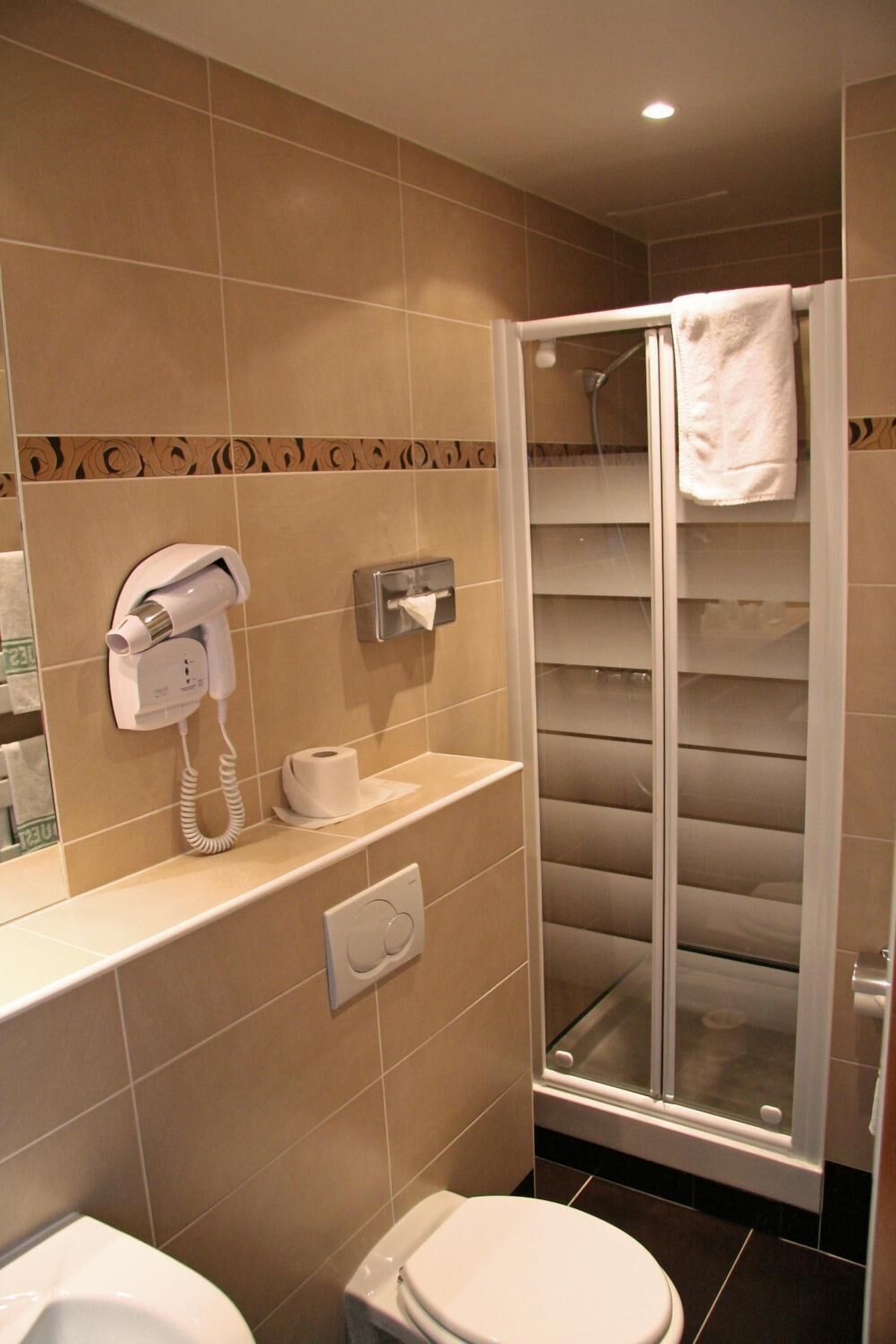 Ein Badezimmer mit Toilette, einer Duschkabine, einem Handtuchhalter und einem an der Wand befestigten Föhn.
