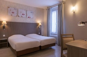 A hotel room with two beds, a wooden table, and two wall-mounted lamps. - L'Ouest Hôtel (Paris)