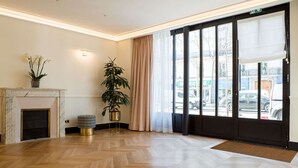 A spacious lobby with a marble fireplace, a potted plant, and a large window with curtains. - Hotel Léna Paris (Paris)