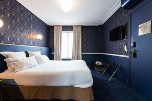 Habitación de hotel con una cama grande, un televisor montado en la pared y una ventana con cortinas.