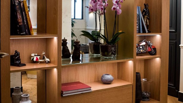 A wooden bookshelf with various items including books, a vase with orchids, and decorative objects. - Hotel Léna Paris (Paris)