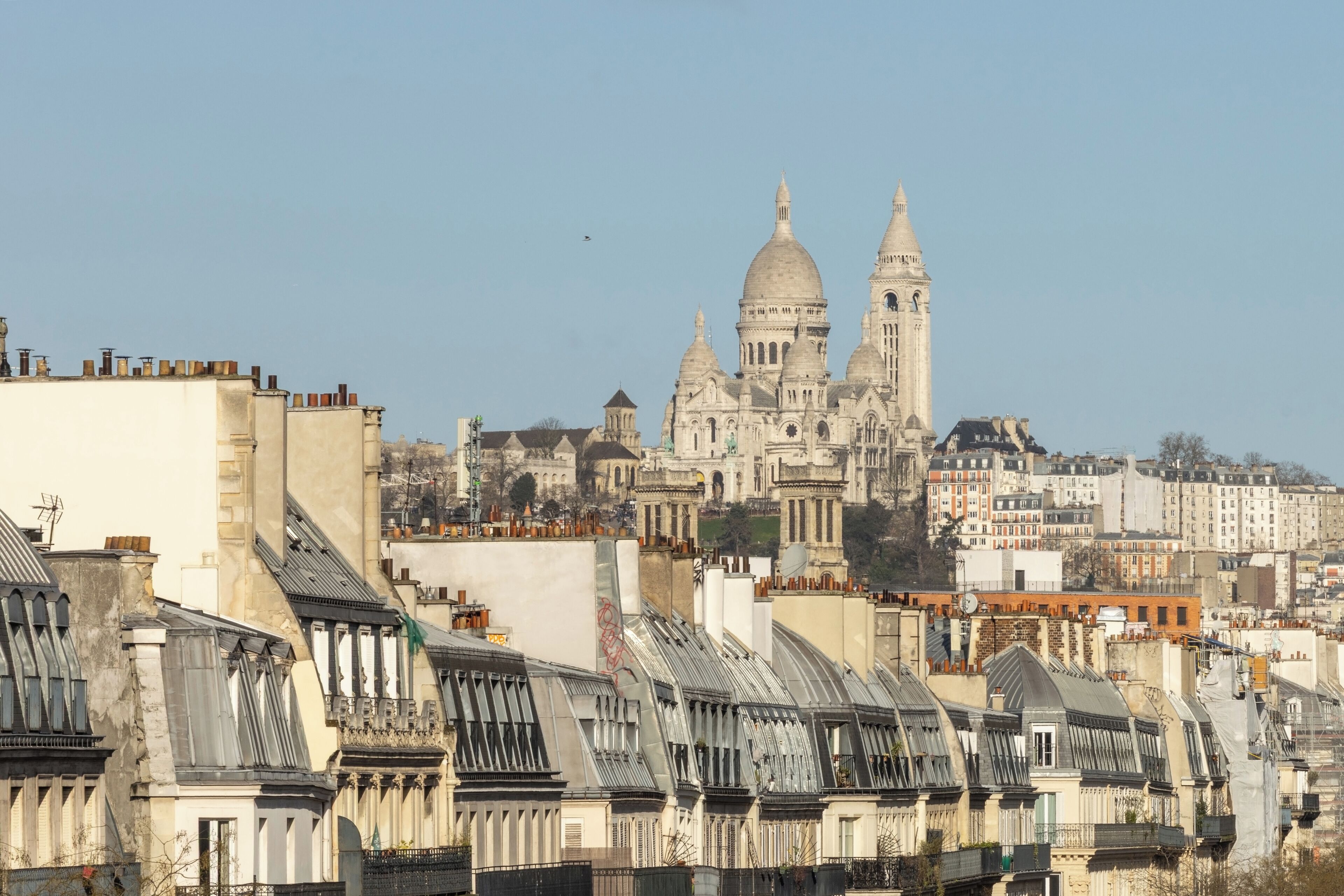 Un paysage urbain dominé par une imposante cathédrale à deux coupoles et un haut clocher, entourée de bâtiments densément regroupés aux toits de formes variées.