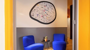 Une pièce avec deux chaises bleues, une petite table sur laquelle se trouve un cactus, et un mur orné d’un motif circulaire.