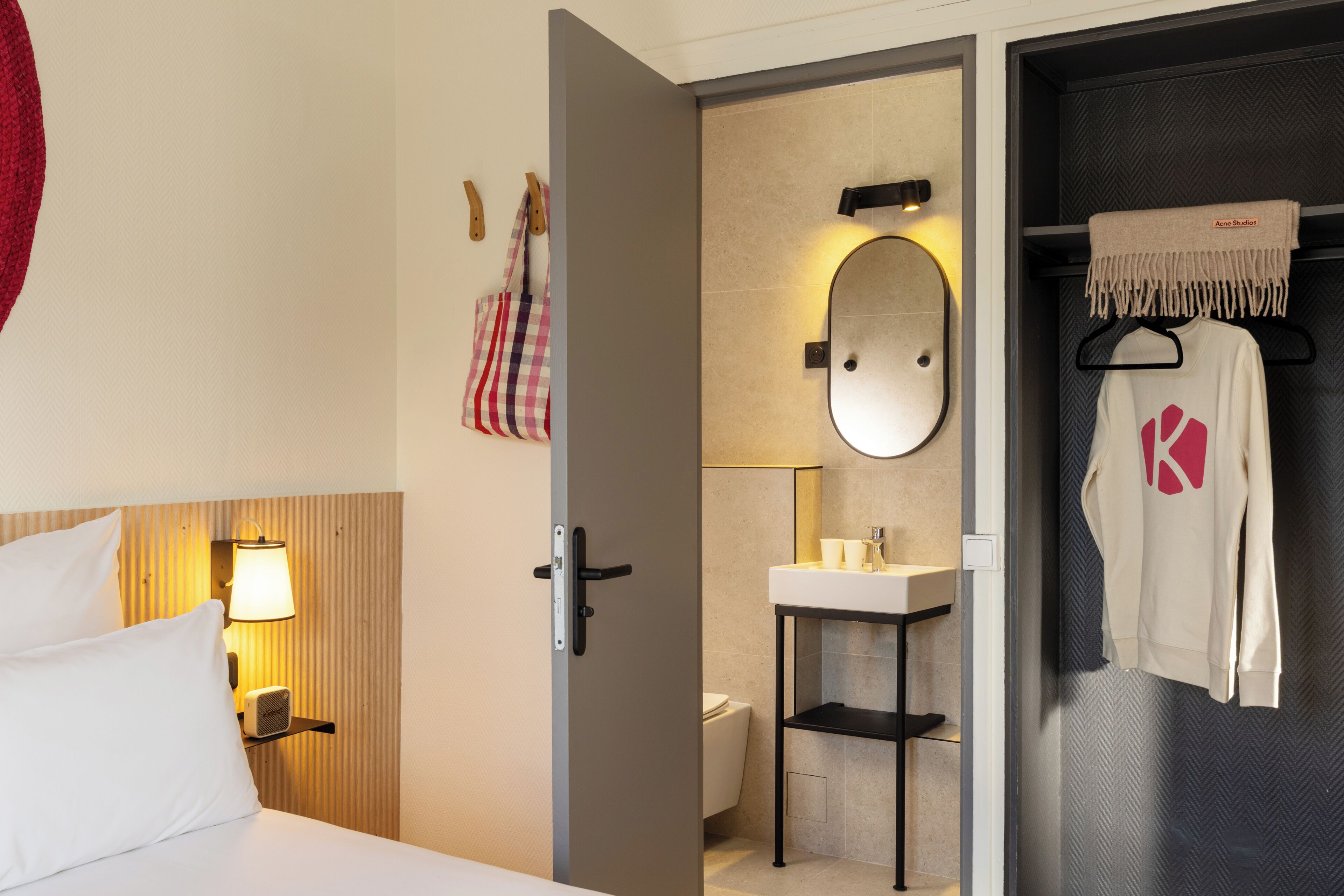 A hotel room with a bed, a bedside lamp, a bathroom with a mirror, a sink, and a towel rack.