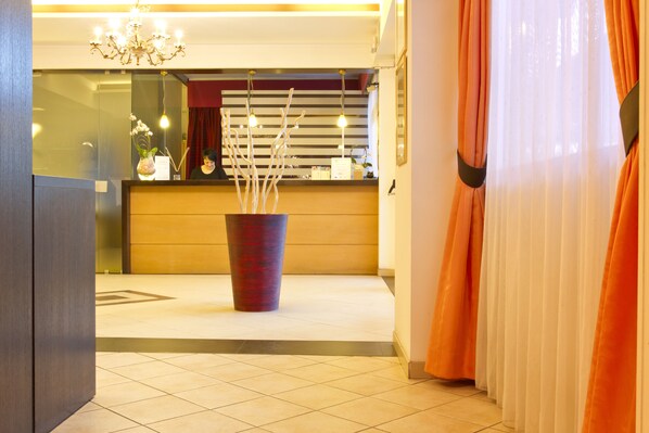 A reception area with a large vase of branches, a reception desk, and a chandelier.