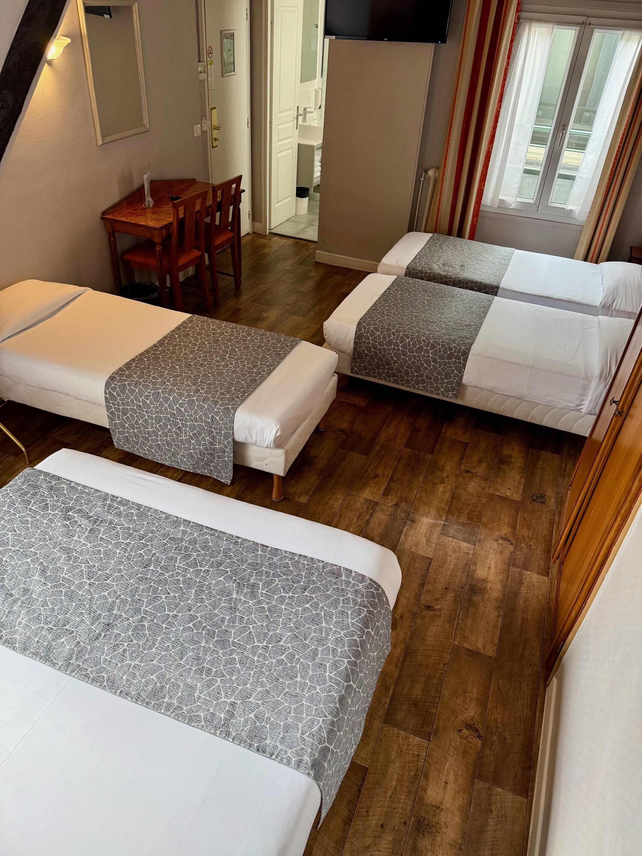 A room with three beds, a wooden table, and a television.