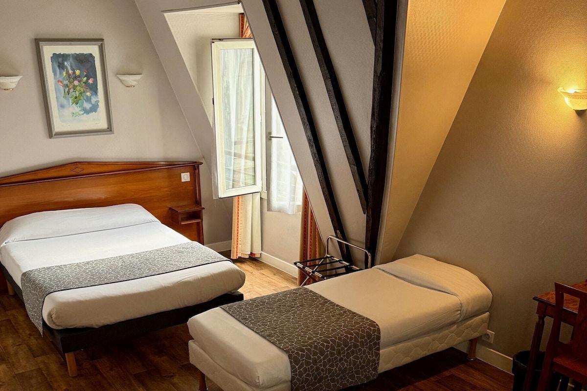 A room with two beds, a wooden headboard, a small table, and a chair.