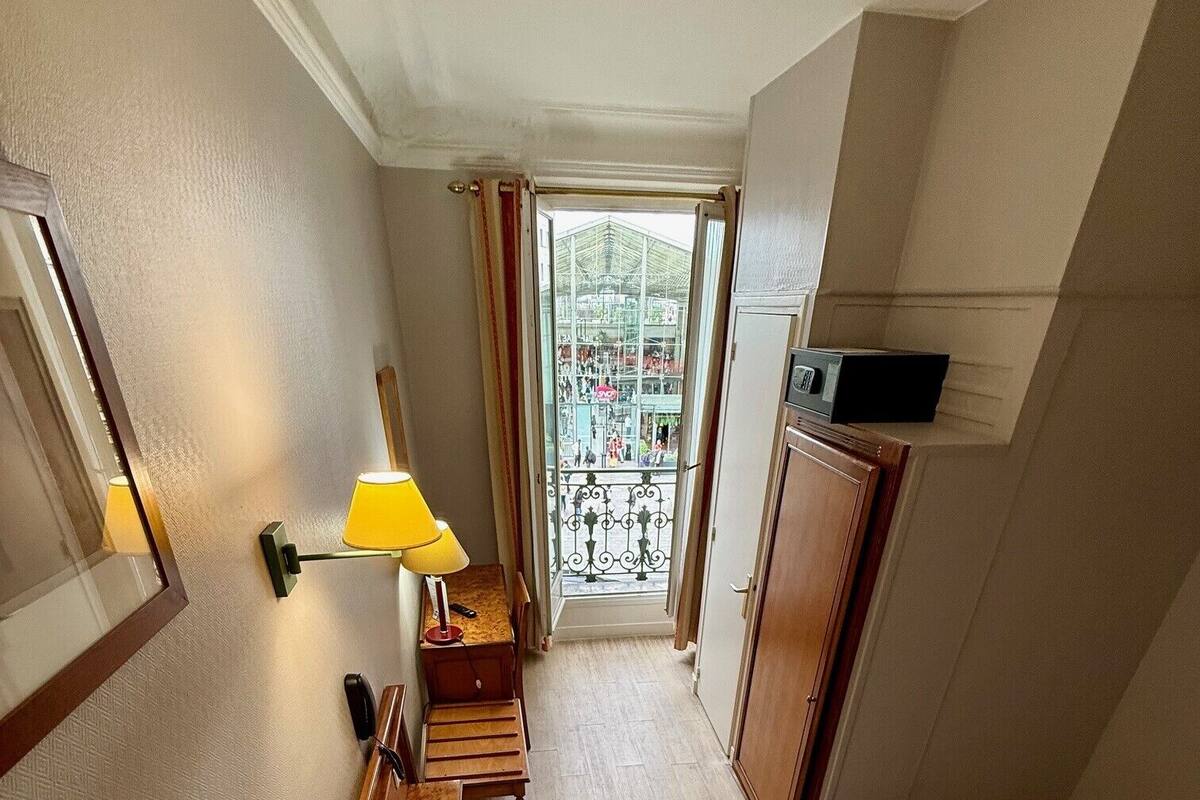 A hotel room with a bed, a desk with a lamp, a wardrobe, and a view of a balcony.